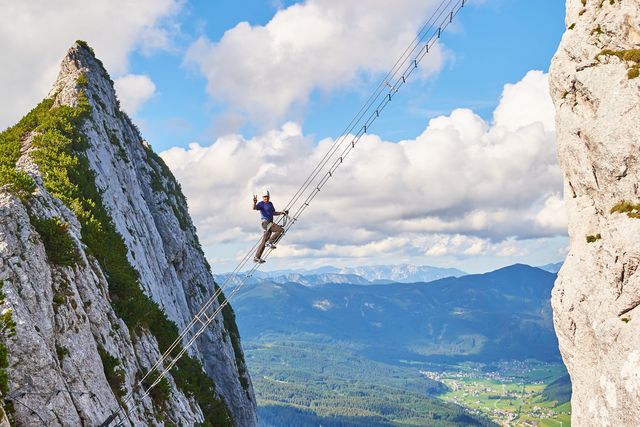 intersport donnerkogel via ferrata in summer, with a man showing a victory sign while climbing the diagonal ladder. stairway to heaven concept.