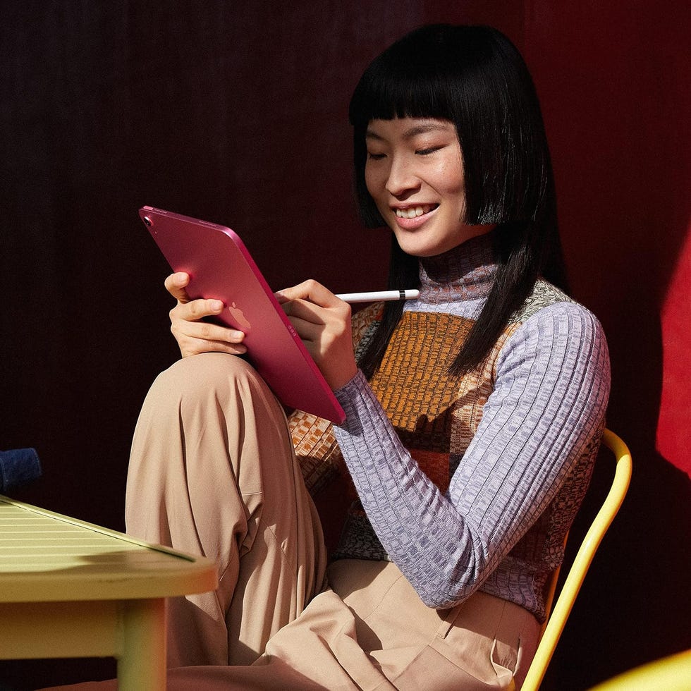 a person sitting on a chair using a stylus with a pink tenth generation ipad