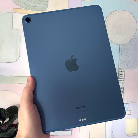 hand holding blue ipad air 5th generation against pastel painting