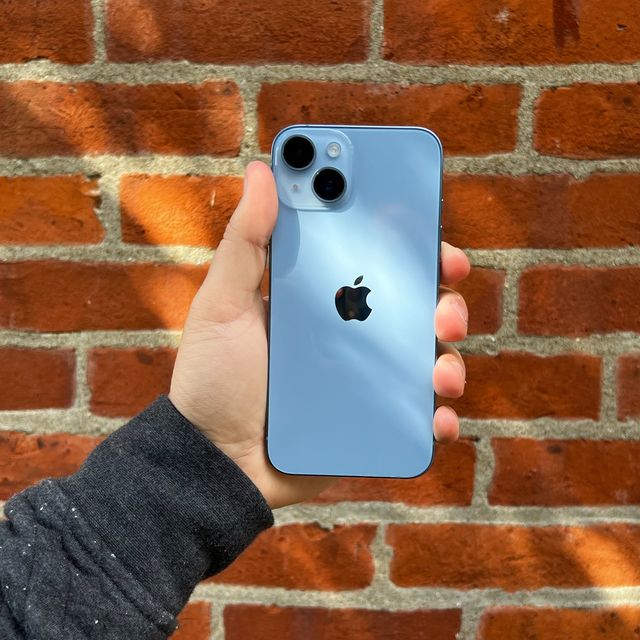 holding blue iphone 14 in front of brick wall