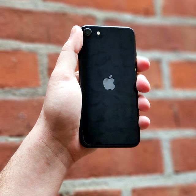 hand holding black iphone se against a brick wall