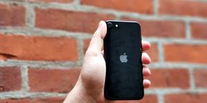 hand holding black iphone se against a brick wall