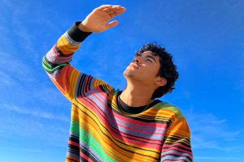 person in striped sweater shielding face from sun against bright blue sky