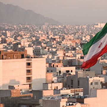 iranian flag waving with city skyline on background in tehran, iran