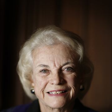 sandra day o'connor smiles at the camera, she wears a purple outfit, a silver necklace, and large earrings