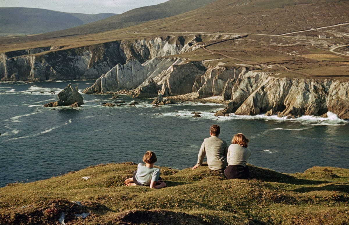 Mensen ontspannen bij Ashleam Bay op het Achill eiland van Ierland op een foto uit een National Geographic van 1940 In de verte zorgt een lage muur ervoor dat koeien en schapen niet van de klif af kunnen vallen