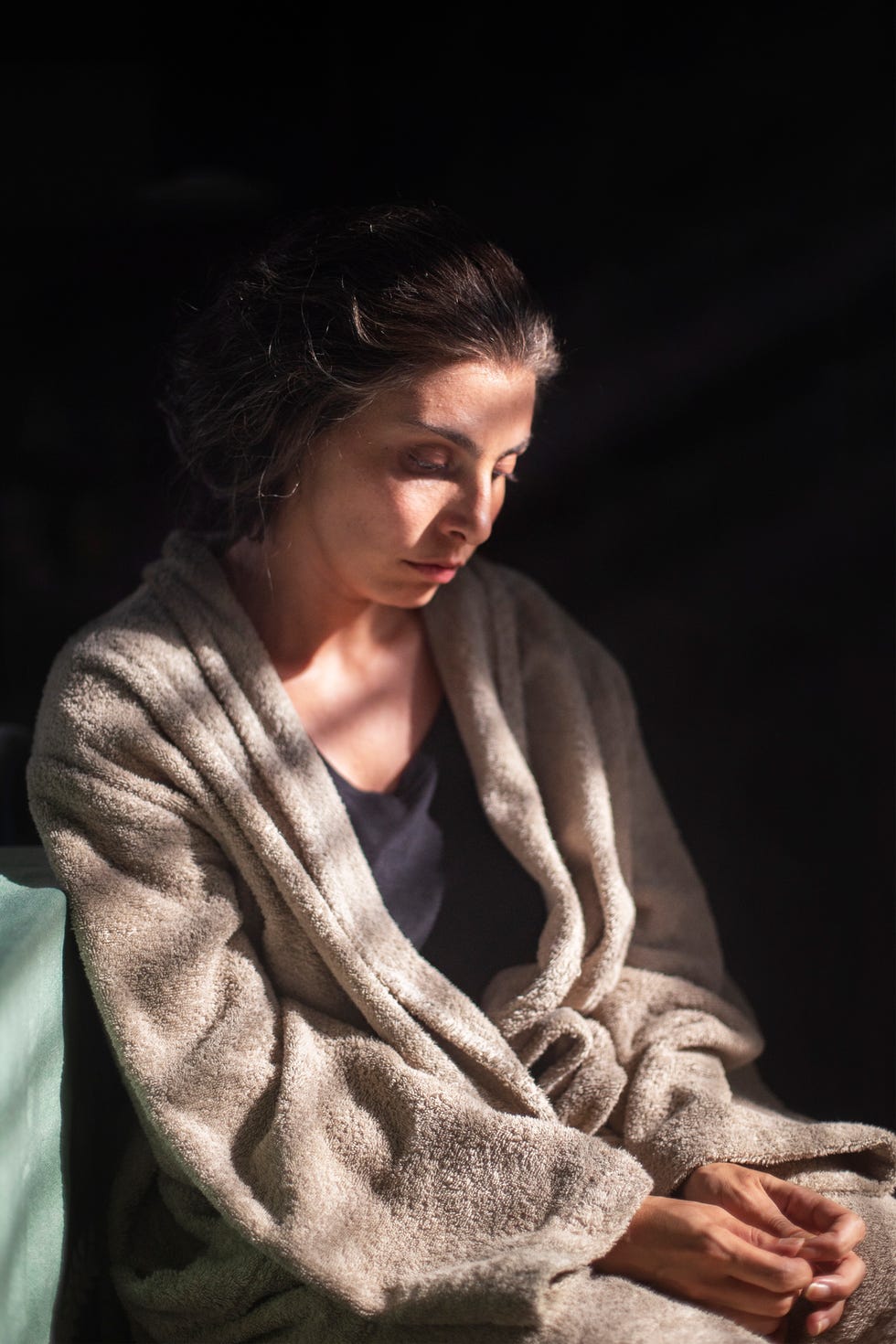 person seated wrapped in a blanket in a dimly lit setting