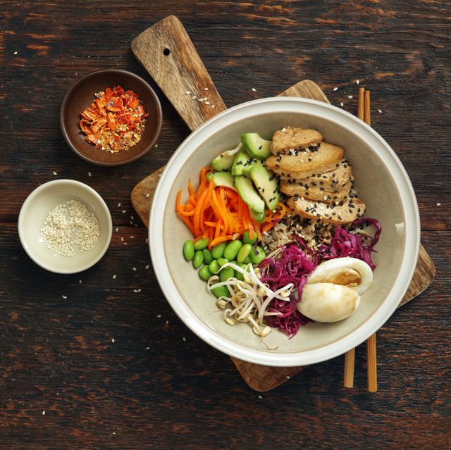 iron rich foods, vegan poke bowl aka tofu poke bowl with tender tofu, red cabbage, carrot, avocado, edamame and bean sprout on a bed of brown rice flat lay top down composition on dark wooden background horizontal image with copy space