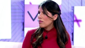 woman in a red sweater with long black hair seated in front of a modern backdrop