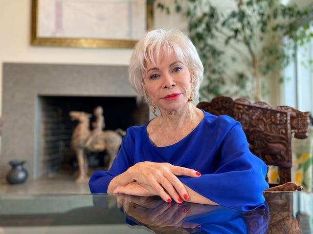la escritora, sentada en su salón, con una blusa azul y el pelo blanco