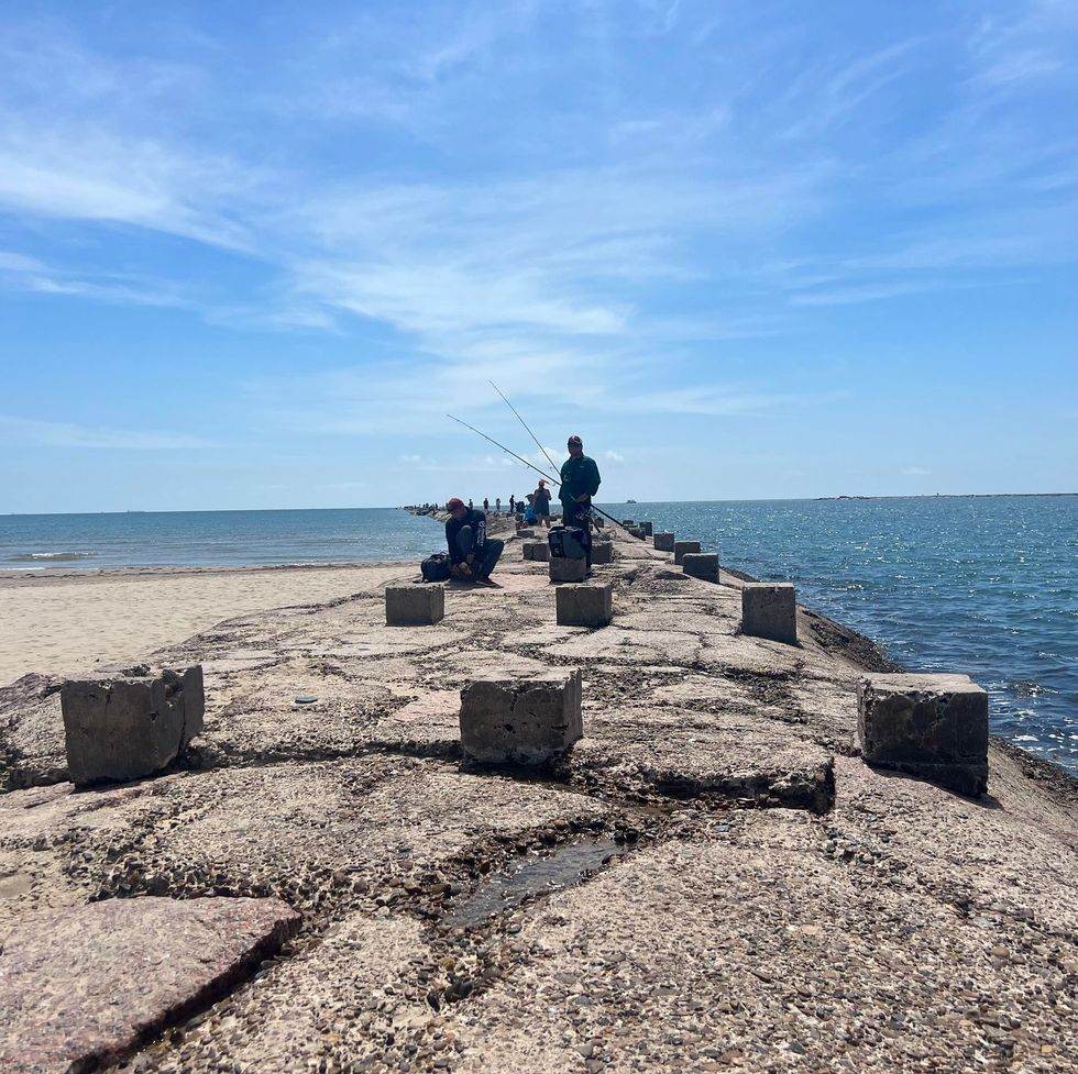 men fishing on the rocks above the ocean at isla blanca park on south padre island