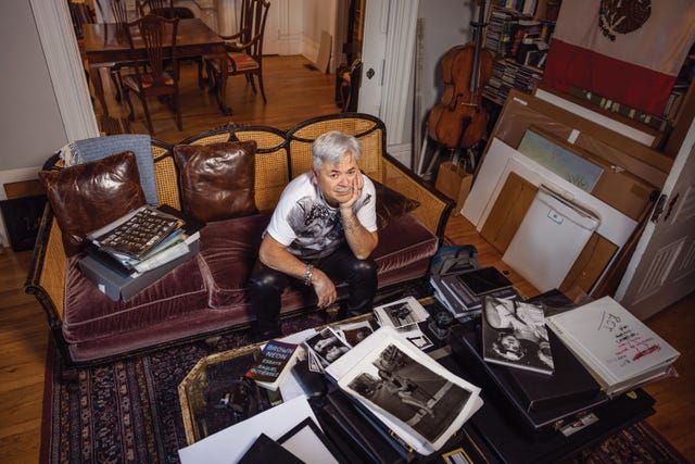 reynaldo rivera sits on a red velvet couch surrounded by prints, cameras, and lightboxes inside his lincoln heights apartment studio.