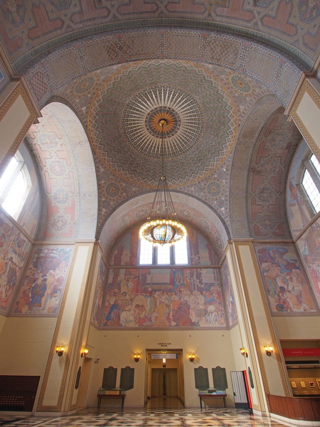 interior of the los angeles central library’s rotunda, with frescoed walls and a glowing art deco chandelier suspended from a mosaic tiled dome.