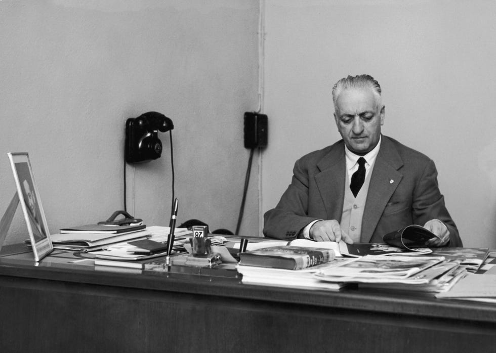 enzo ferrari looking through items while sitting at his office desk