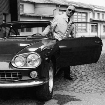 enzo ferrari looking ahead at a camera as he opens a car door to exit