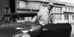 enzo ferrari looking ahead at a camera as he opens a car door to exit