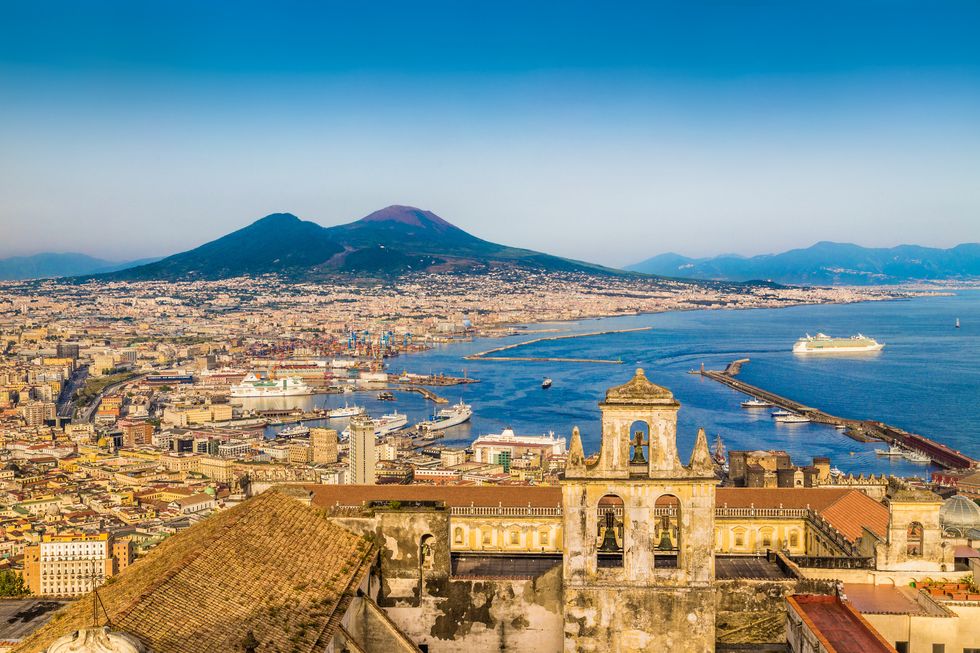 scenic picture postcard view of the city of napoli naples with famous mount vesuvius in the background in golden evening light at sunset, campania, italy