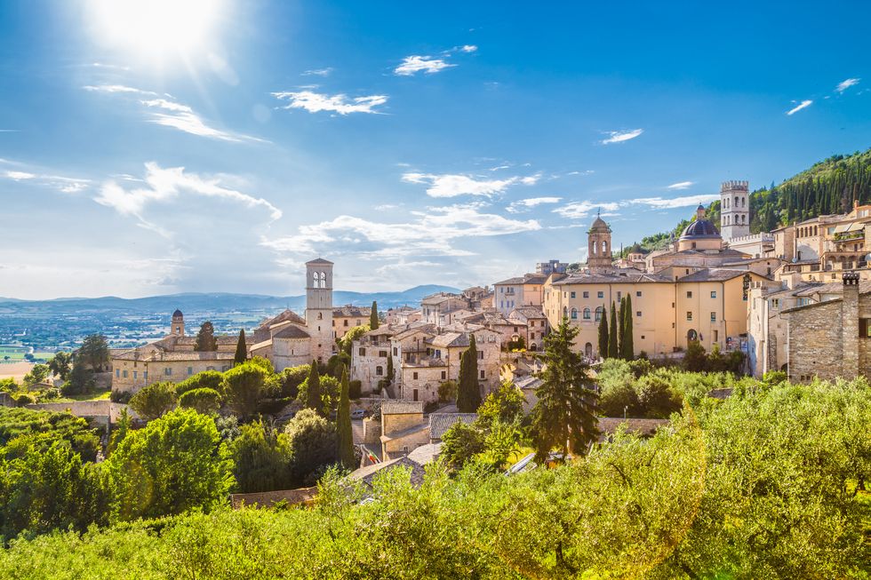 panoramic view of the historic town of assisi on a beautiful sunny day with blue sky and clouds in summer, umbria, italy