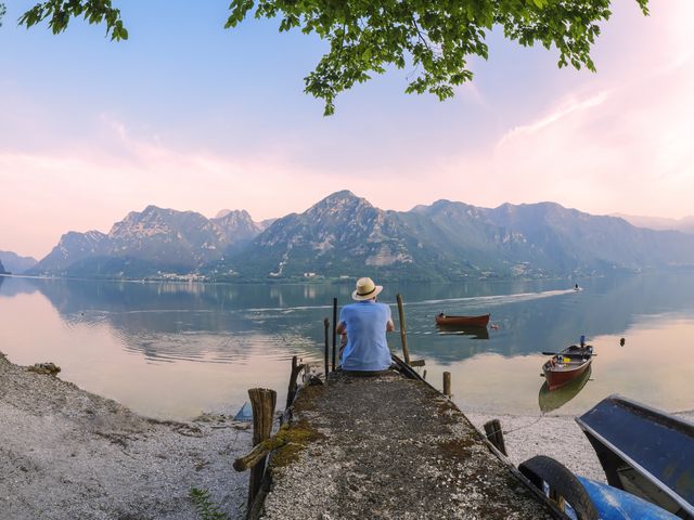 italy, lombardy, back view of man sitting on jetty at lake idro at morning twilight