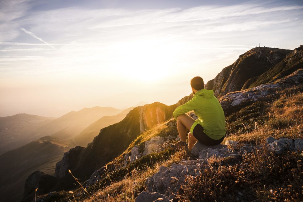italy, mountain running man sitting on rock looking at sunset