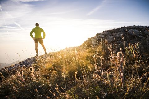Italy, mountain running man standing on trail looking at sunset