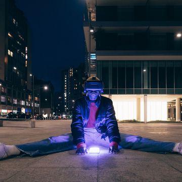 italy, woman withvr goggles sitting on sidewalk in city at night