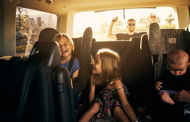3 kids in the back seat of a car as dad closes the trunk