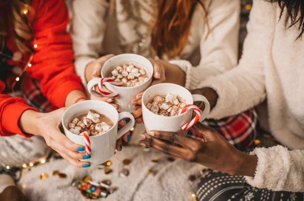three hands holding three cups of hot cocoa with candy canes