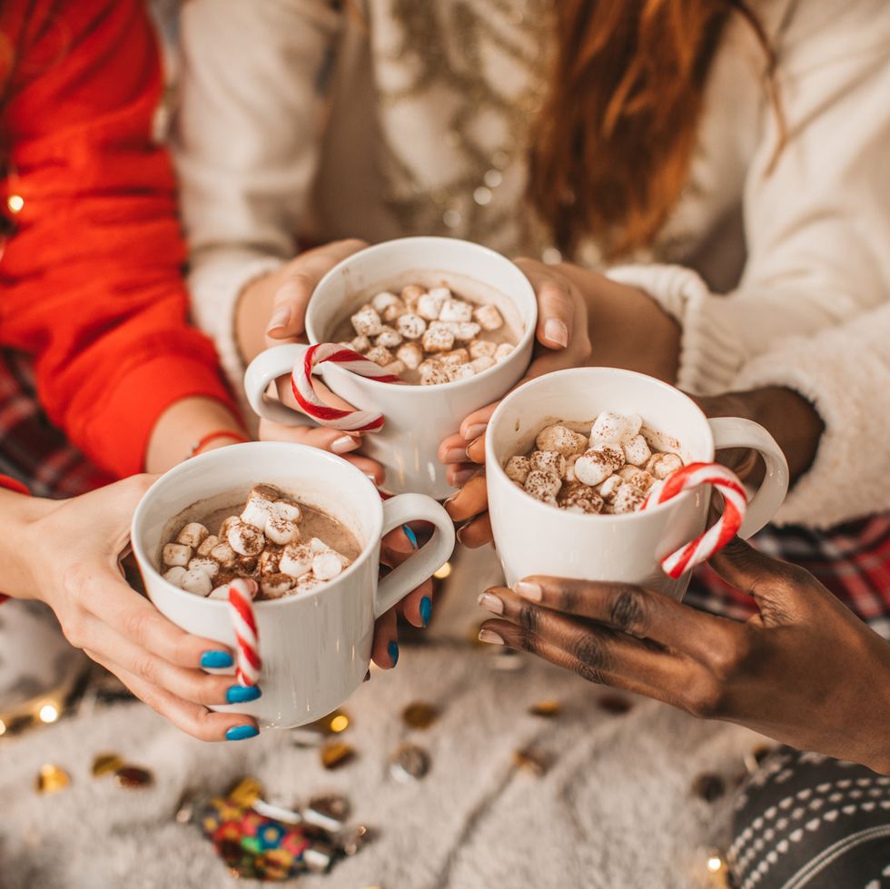 three hands holding three cups of hot cocoa with candy canes