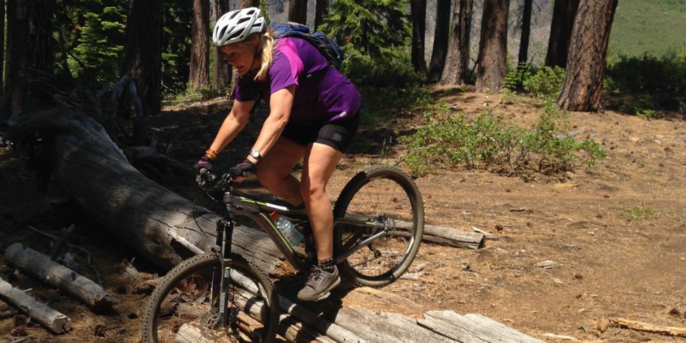 women riding mountain bike over logs