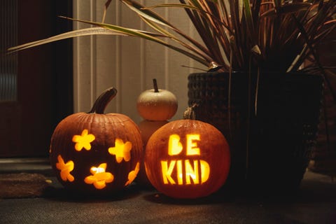 jack o lantern pumpkins illuminated outside a house at night, one with flower cutouts and the other with the words be kind