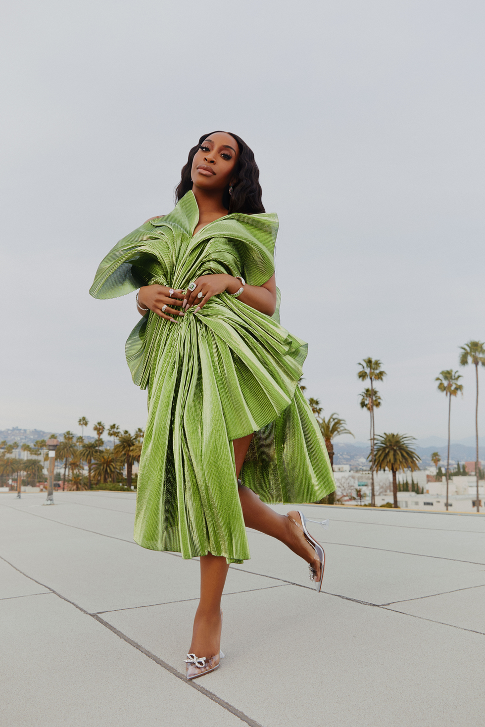 jackie aina in a green dress with palm trees and hills in the background