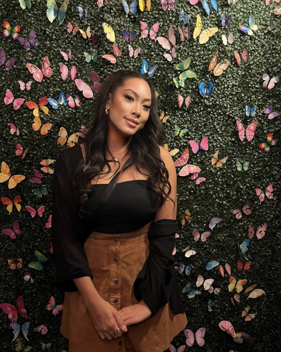 a woman posing in front of a wall of flowers