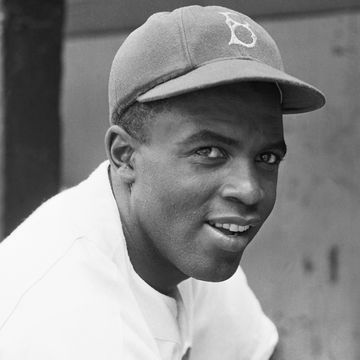 jackie robinson smiling while looking toward the camera and wearing his brooklyn hat