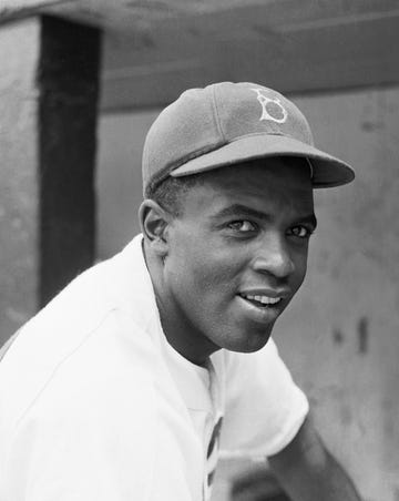 jackie robinson smiling while looking toward the camera and wearing his brooklyn hat