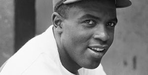 jackie robinson smiling while looking toward the camera and wearing his brooklyn hat