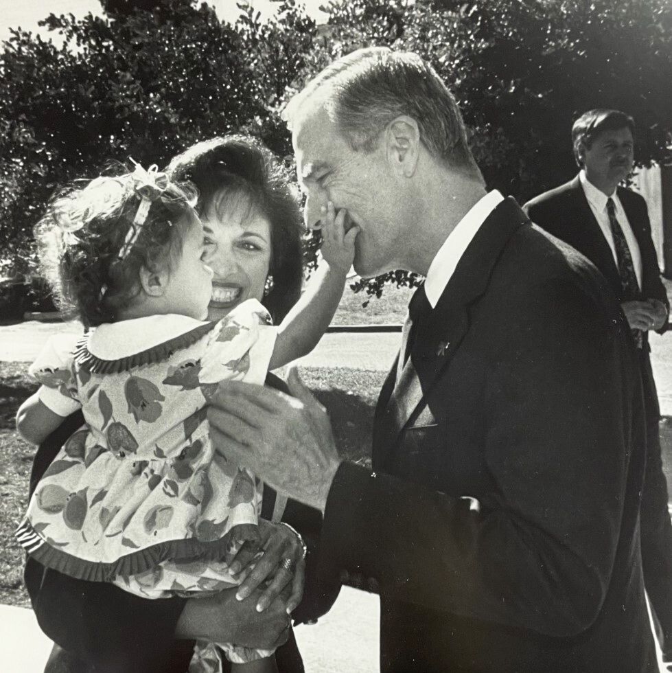 speier holding her toddler daughter who is touching pete wilson's face