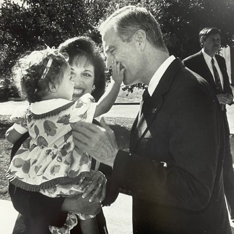 speier holding her toddler daughter who is touching pete wilson's face