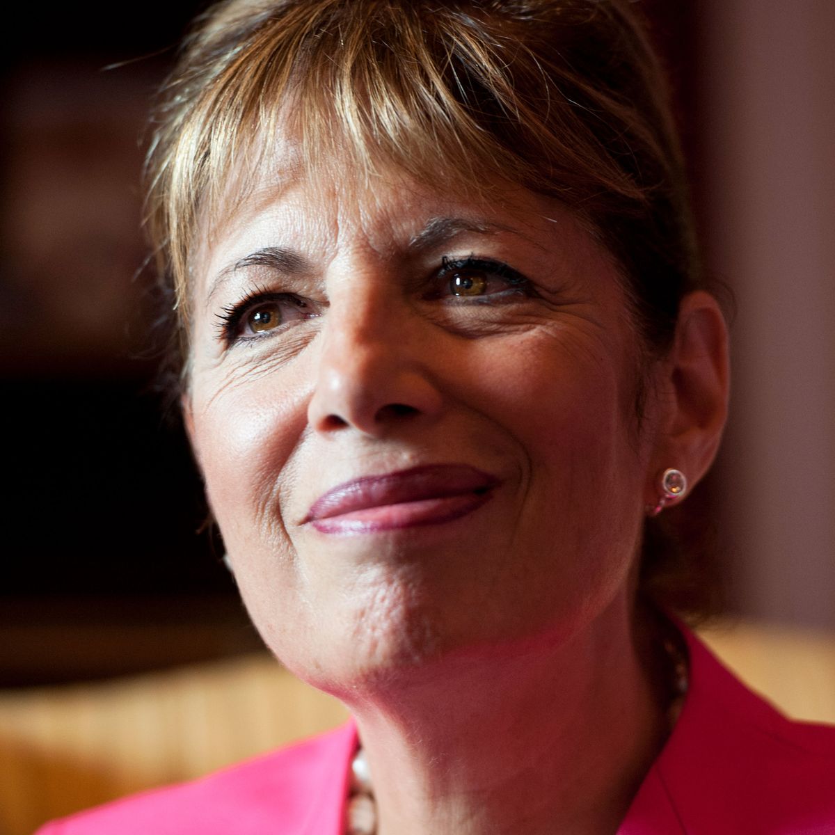 jackie speier wearing a black shirt, pink suit jacket, a white necklace and staring just off to the side of the camera