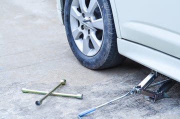 Jacking up a car to change a tyre after a roadside puncture with the hydraulic jack inserted under the bodywork raising the vehicle