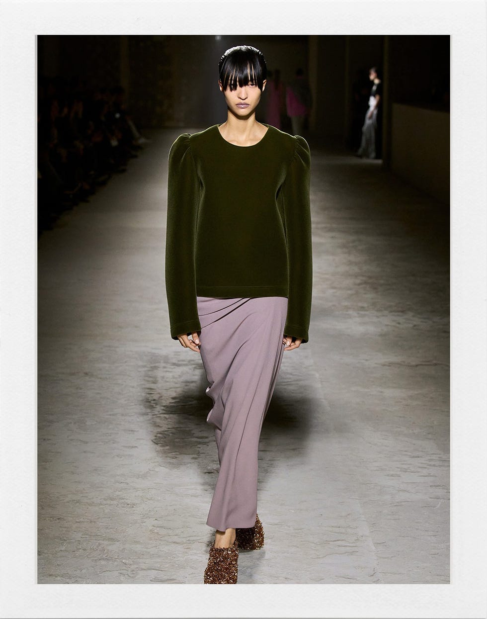a model wearing a green top and lavender skirt on a runway