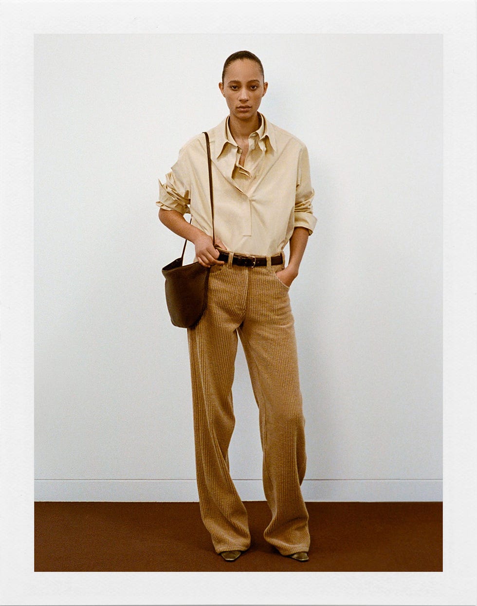 model showcasing a stylish outfit with a beige shirt and striped brown pants