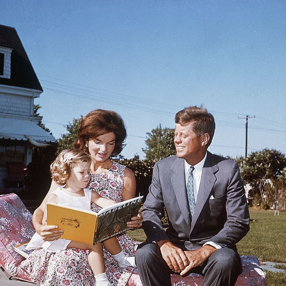 jacqueline kennedy and her husband senator john f kennedy sit on a lounge chair at their summer home jacqueline reads to her daughter caroline from a book