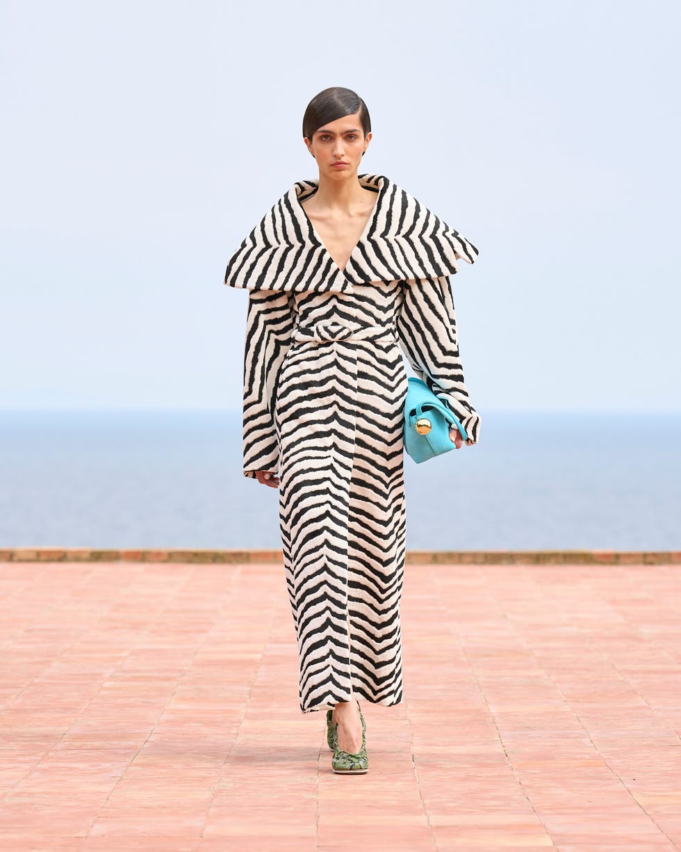 A model wearing a striped outfit carries a turquoise handbag