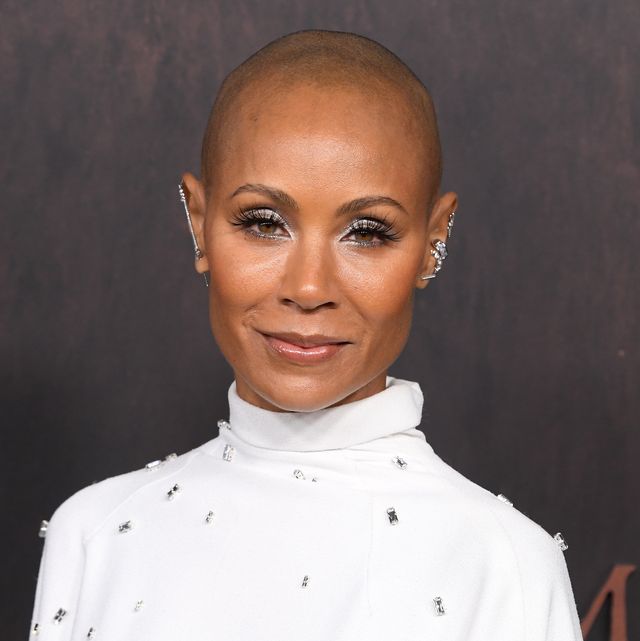 jada pinkett smith smiles at the camera, she wears a white turtleneck dress studded with jewels and several silver and diamond earrings