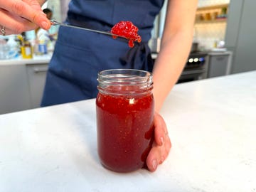 person holding a scoop of jam above a jar of jam