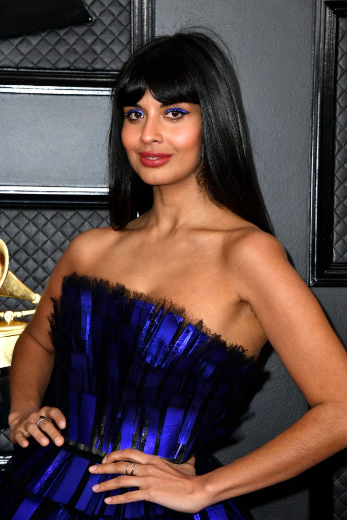 jameela jamil wears a blue and black strapless dress with her hair down on the red carpet
