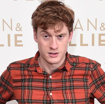 james acaster, a man stands with hands on hips wearing a red check shirt