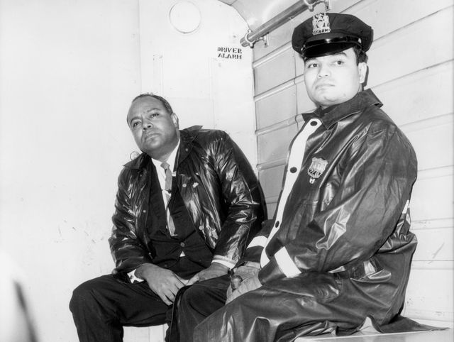 James Farmer, the Executive Director of the Congress for Racial Equality, sits next to a uniformed officer in the back of a police wagon
