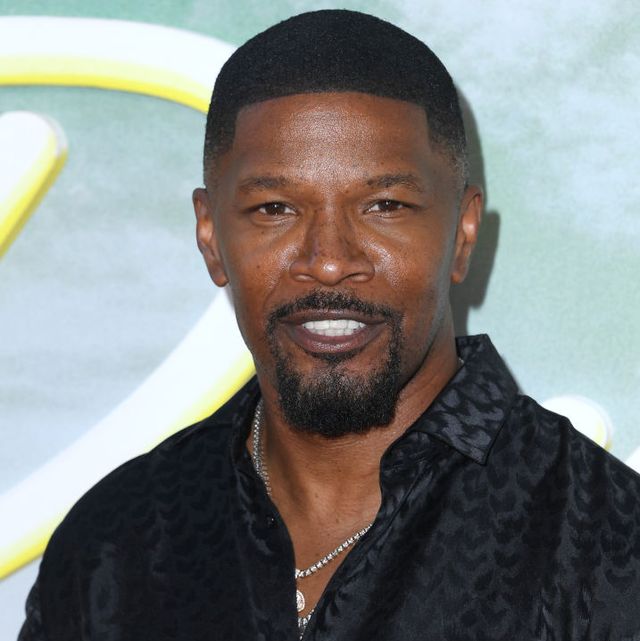 jamie foxx poses for a photo with a slight smile on his face, he wears a black collared shirt that is unbuttoned and two diamond necklaces